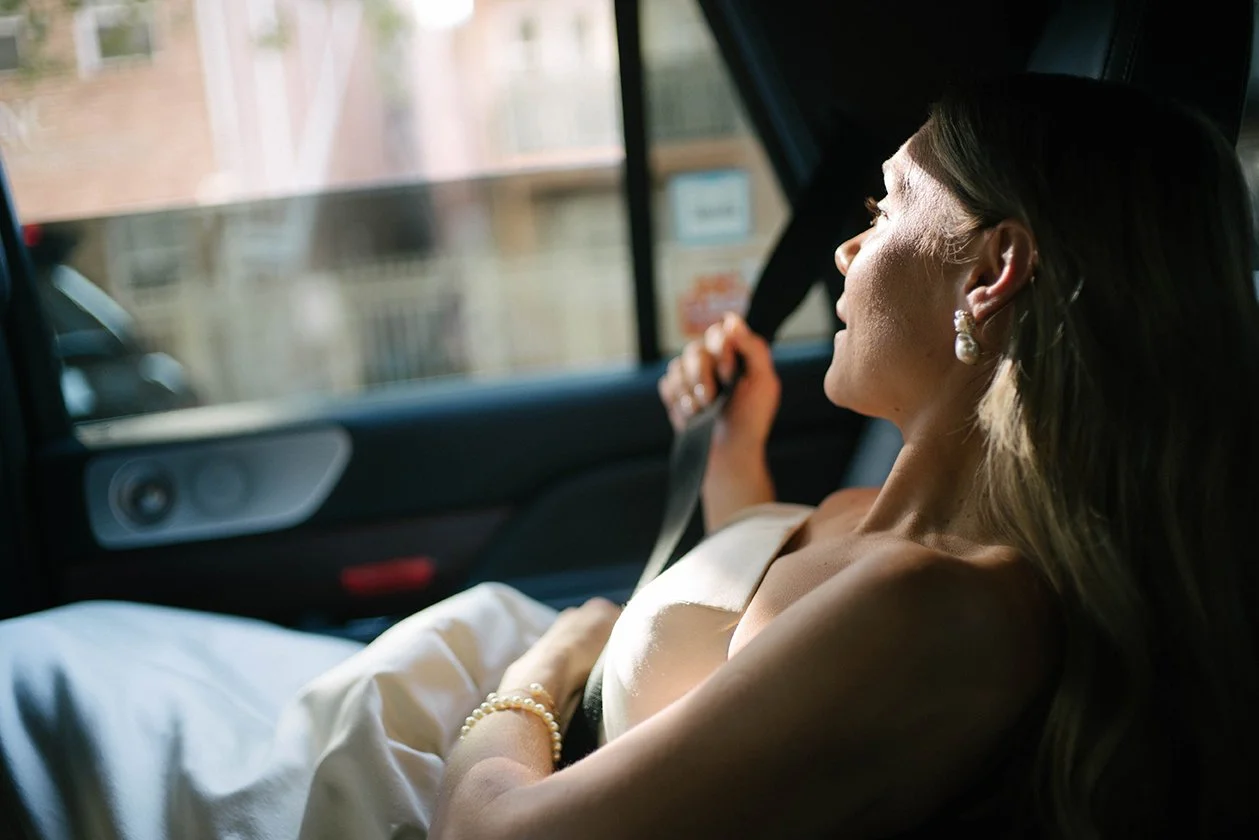 A woman lying on a car seat with sunlight on her face, holding a seatbelt in her hand.
