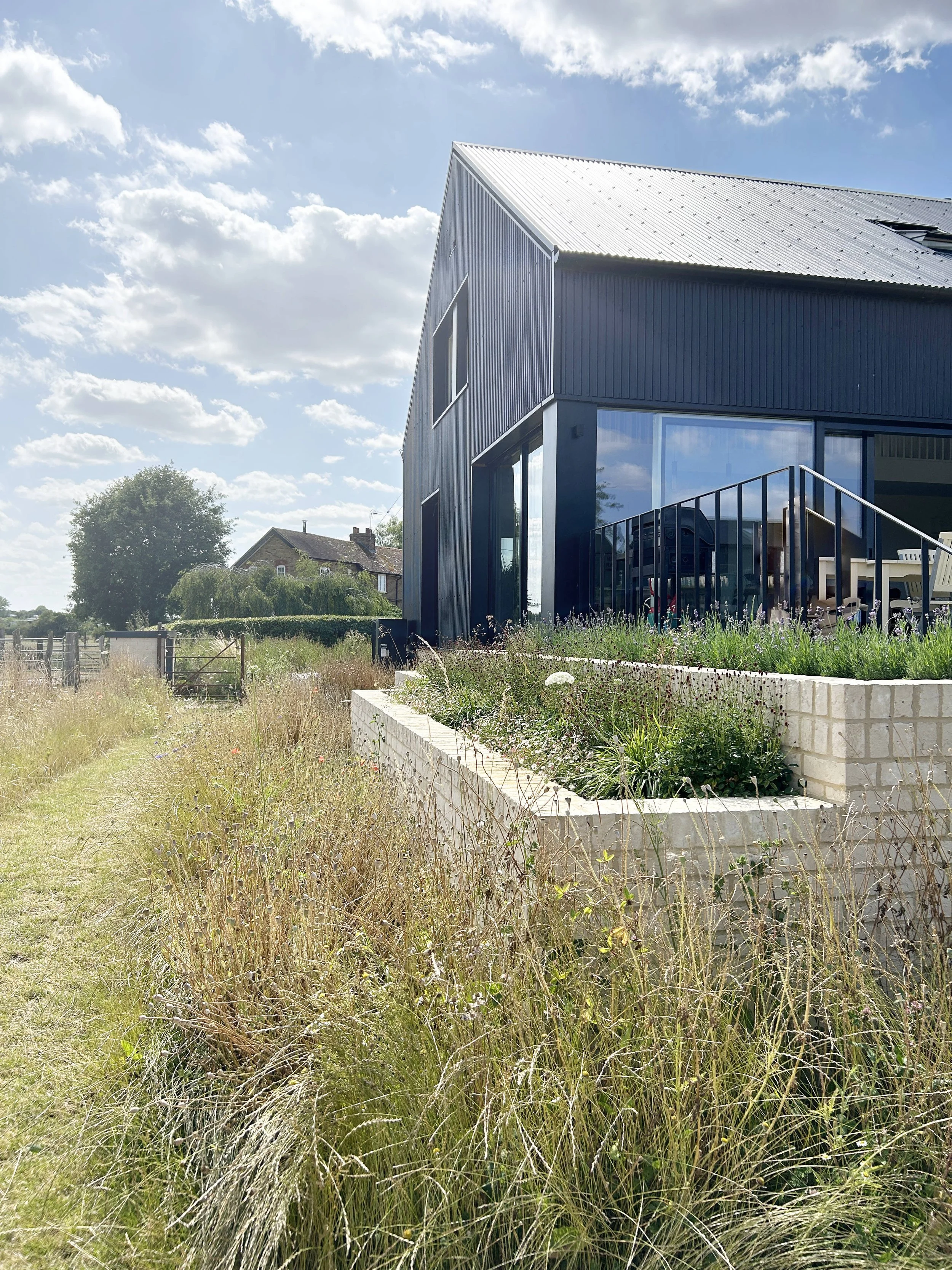 exterior view of grain store new build house project as seen across the meadow grasses.