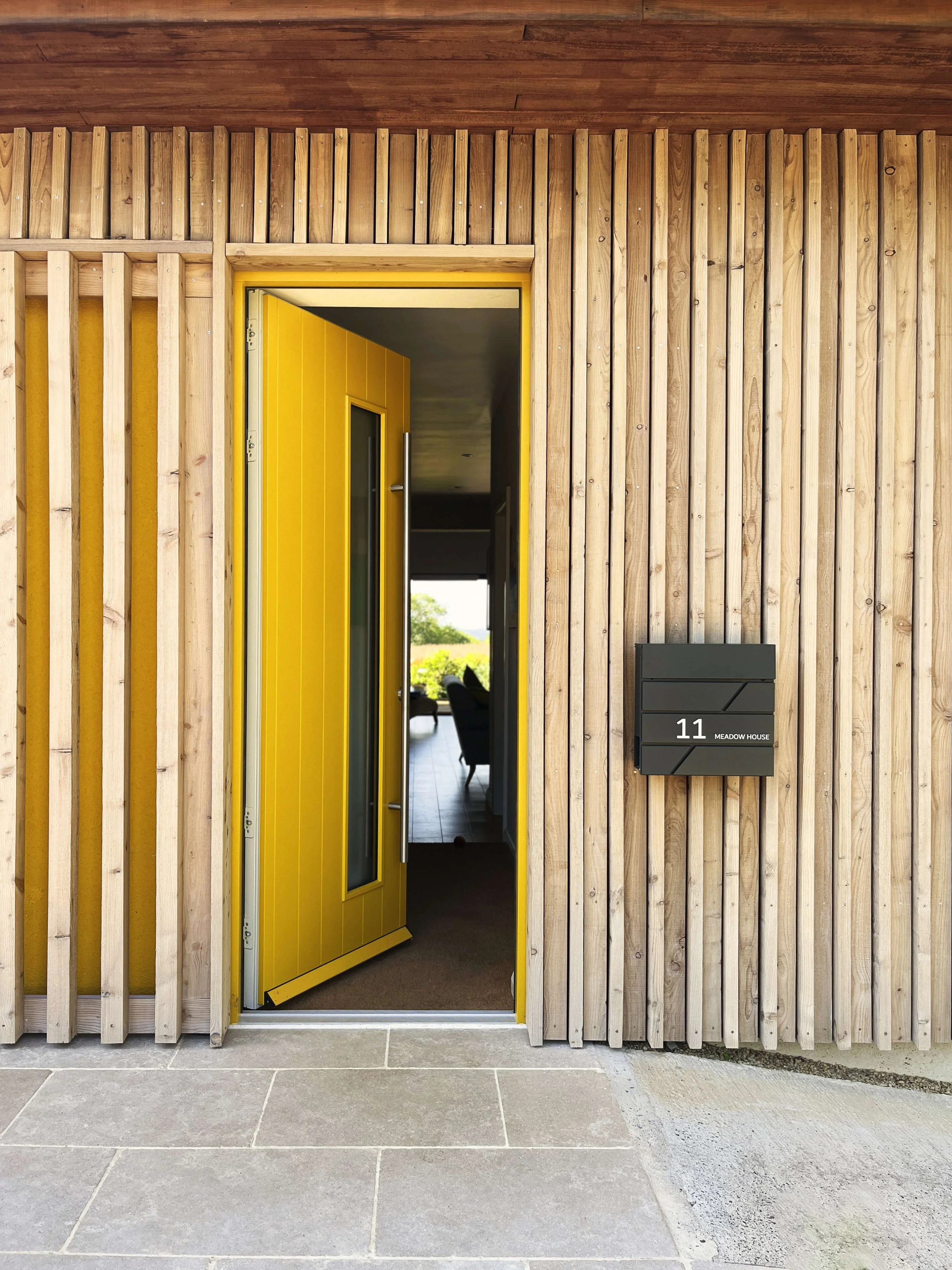 Photo of the new daffodil yellow front door to the bungalow, leading through to views out to the rear garden beyond.