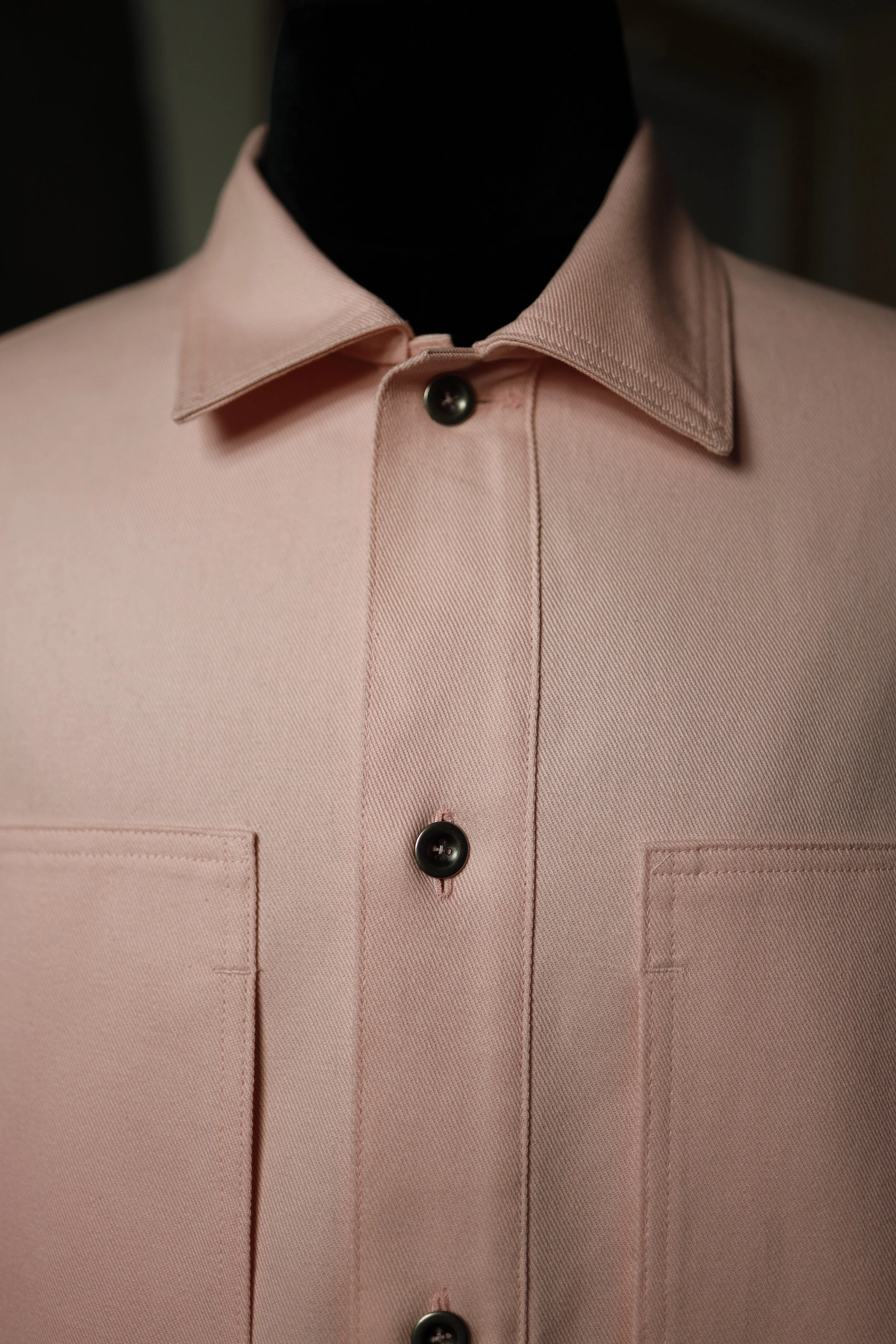 Close-up of a rose pink cotton denim pullover shirt featuring oversized patch pockets, dark buttons, and textured fabric.