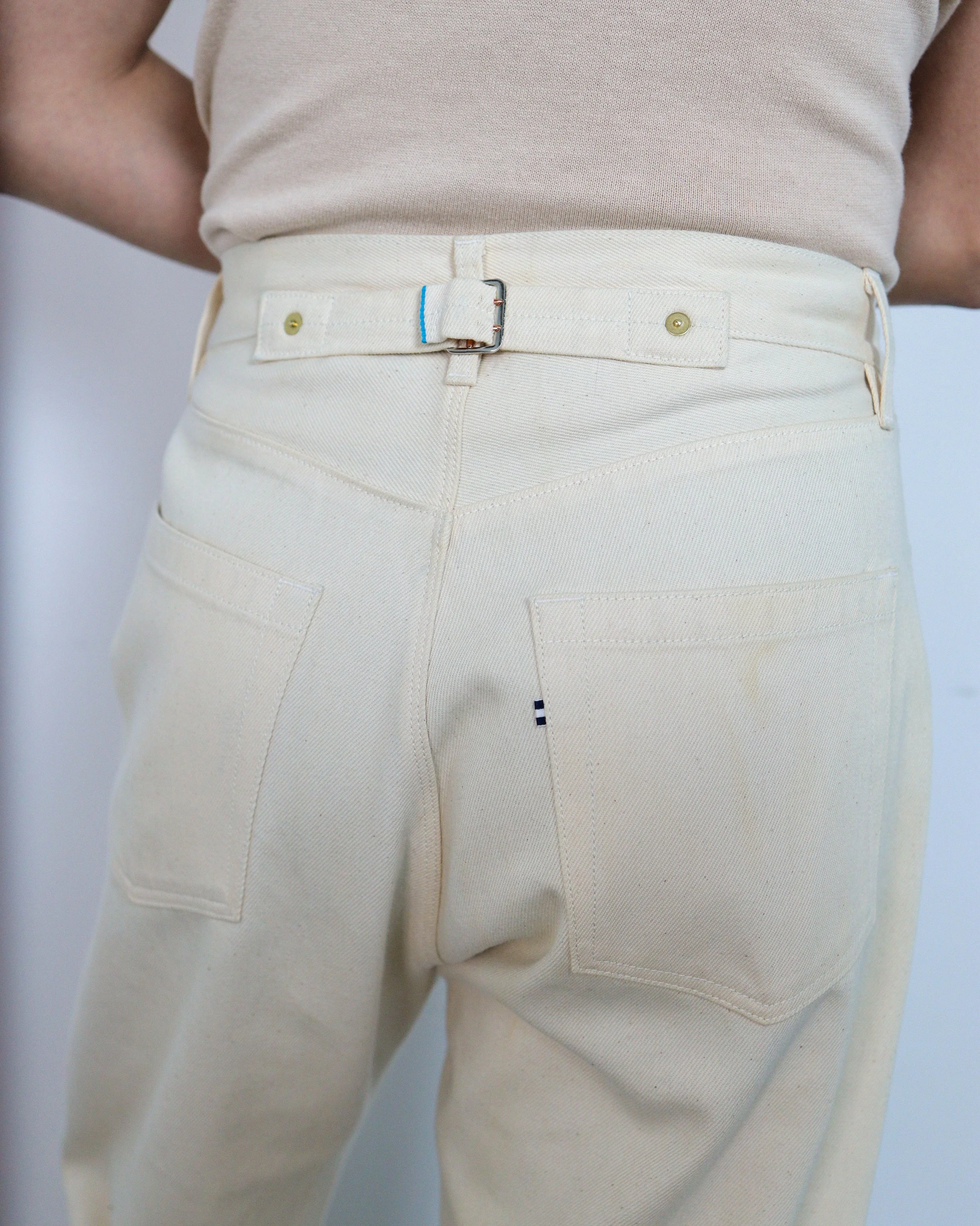 Close‑up detail of the back pocket and waistband on ecru selvedge denim jeans by [ko’lōn], showing construction and hardware details.