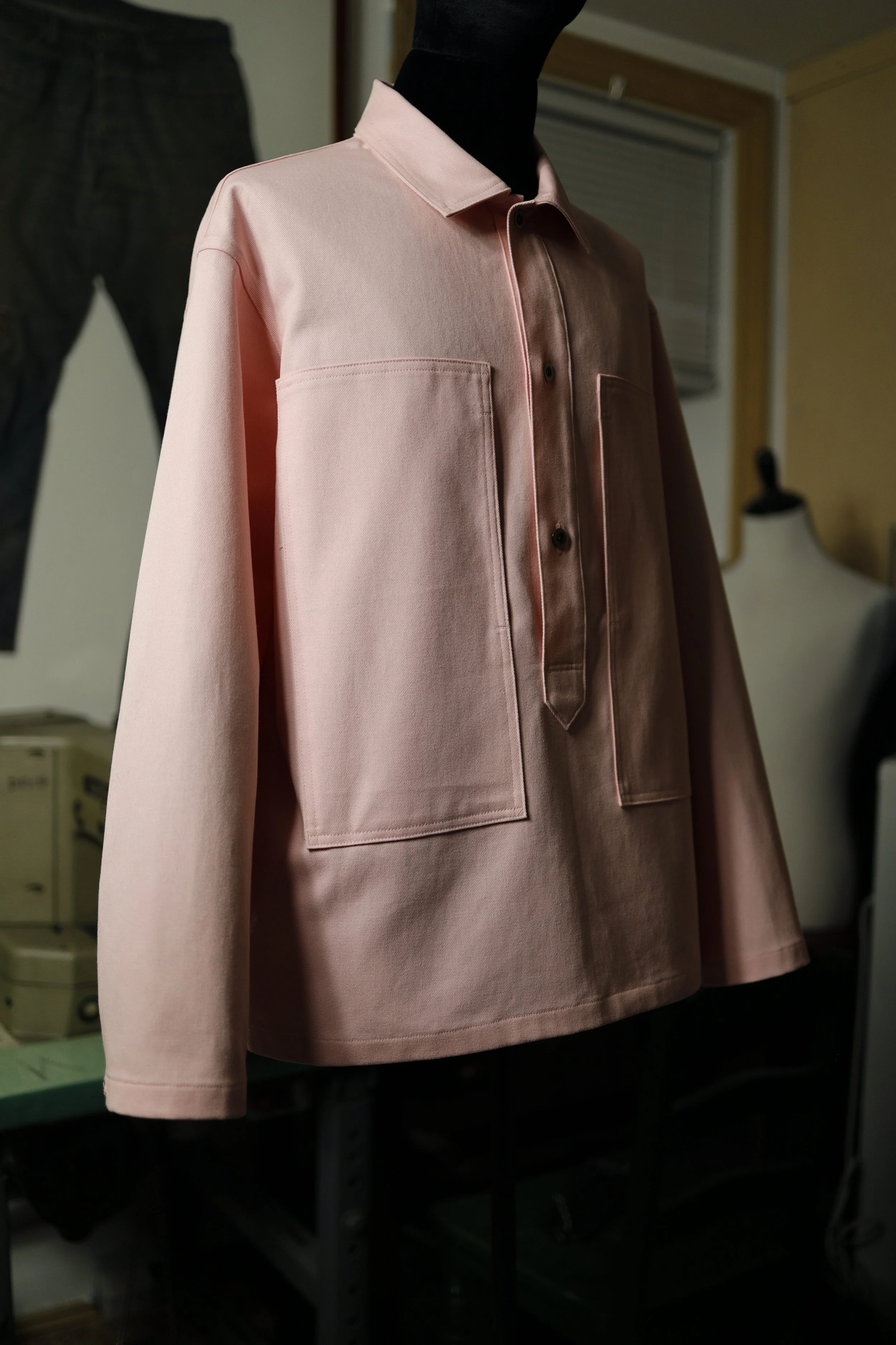 Side view of a rose pink cotton denim pullover shirt with large patch pockets and a relaxed silhouette.