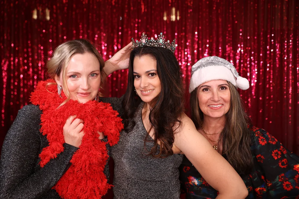 Three guests wearing crowns at a OneAway Studios corporate photo booth with a red sequin backdrop