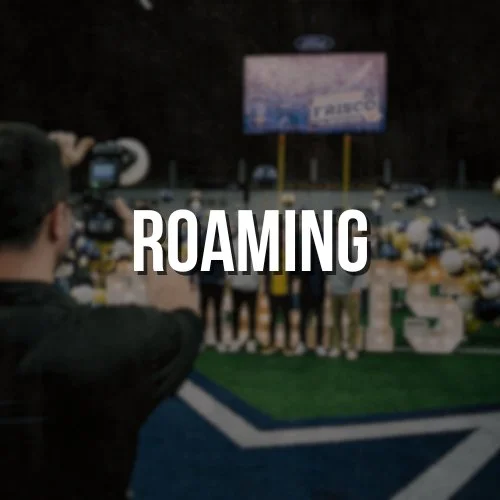 A person taking a photo at a football game with a large screen displaying 'Fresno' in the background.