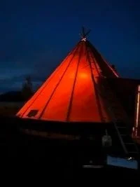 A snowy landscape with a line of sled dog teams and mushers, set against a backdrop of snow-covered mountains and a clear blue sky.