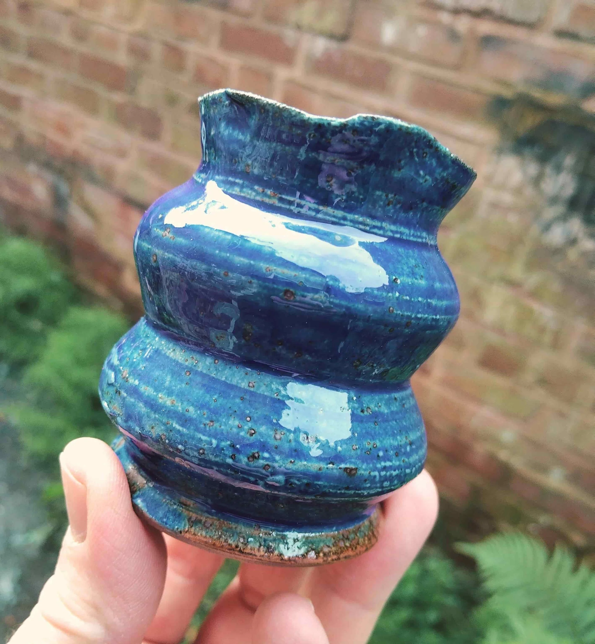 deep blue vase held up wit fingers against brick background in daylight