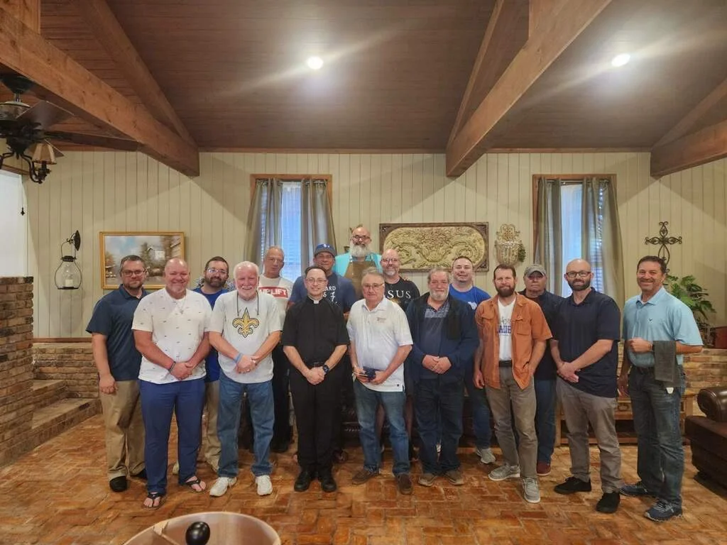 Group of people standing inside a rustic room with brick flooring, wood beams, and artwork on the wall.
