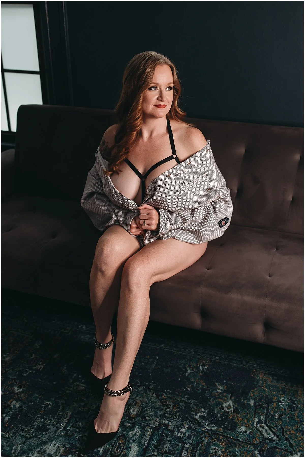 Confidence-focused boudoir session showing a redheaded woman sitting on a couch wearing her partner’s shirt