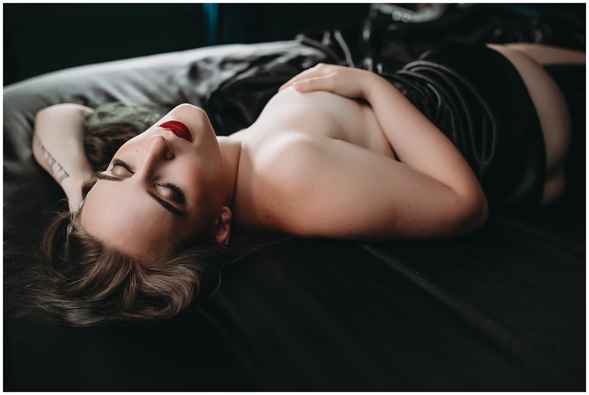 Woman laying down in black satin sheets during her boudoir session in Downtown Jacksonville