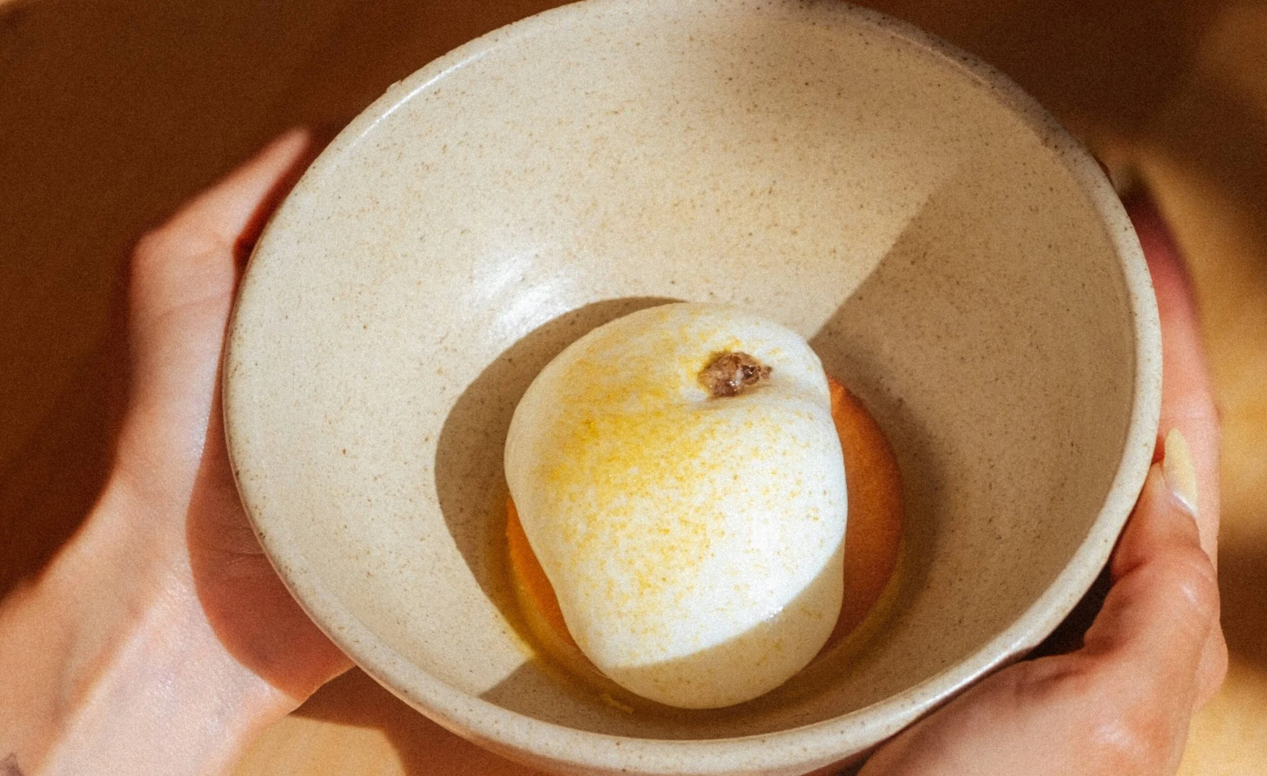 Huevo cocido en un tazón beige, sostenido con ambas manos.