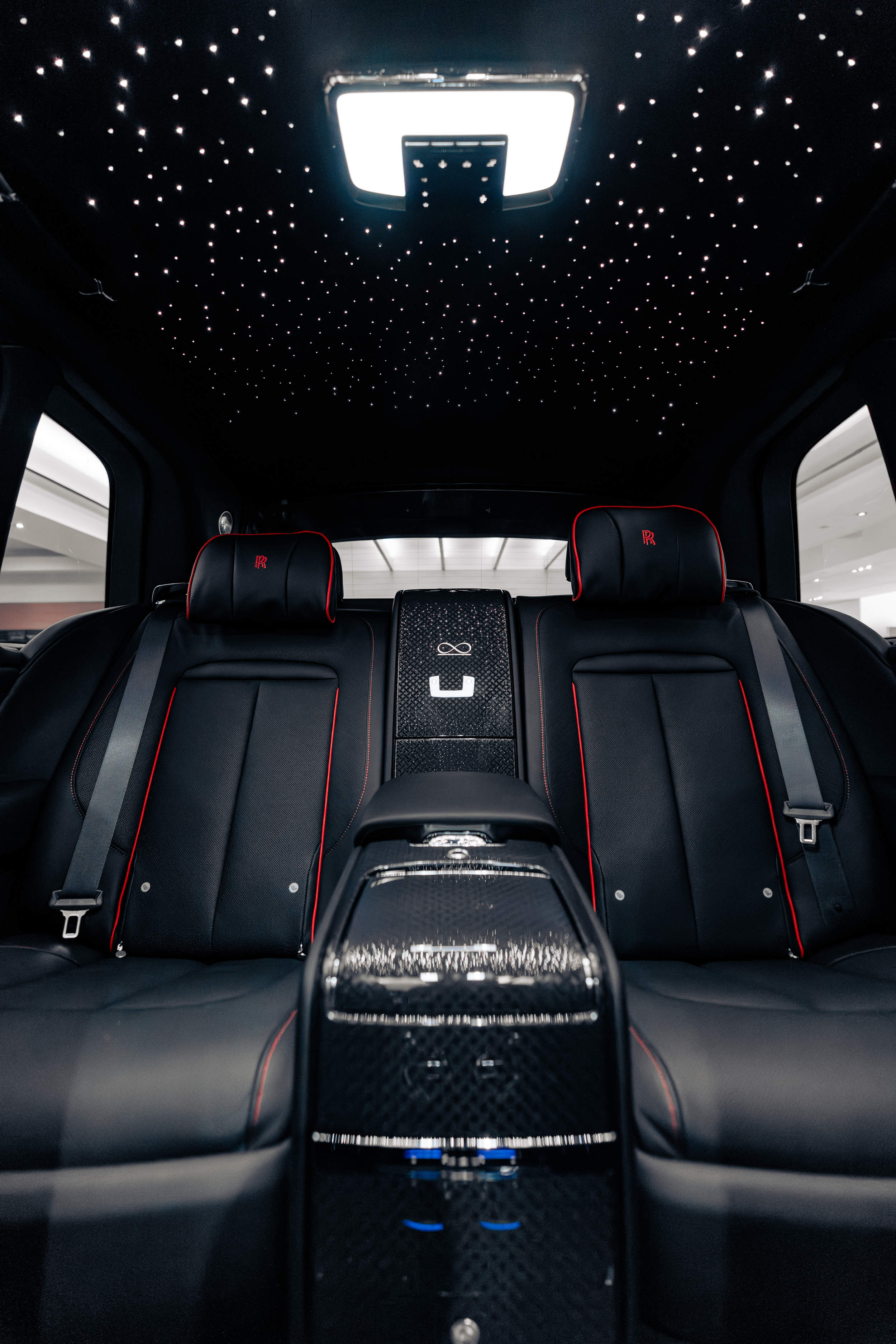 The interior of a luxury car, showing black leather seats with red piping, a starry LED ceiling, and a center console with a digital display.