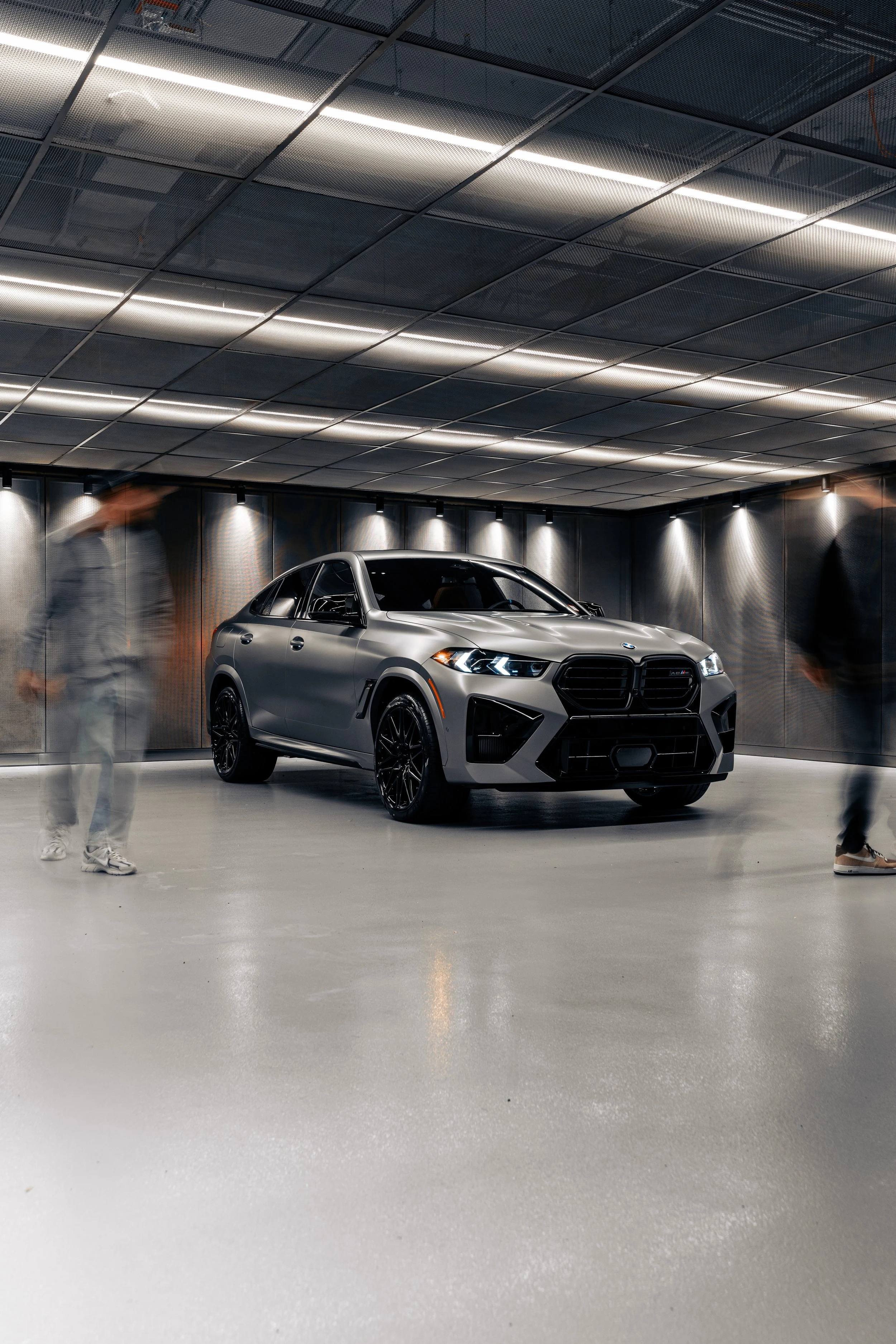 A silver sports utility vehicle (SUV) displayed in a modern showroom with a metallic ceiling and polished floor, with blurry people walking around.