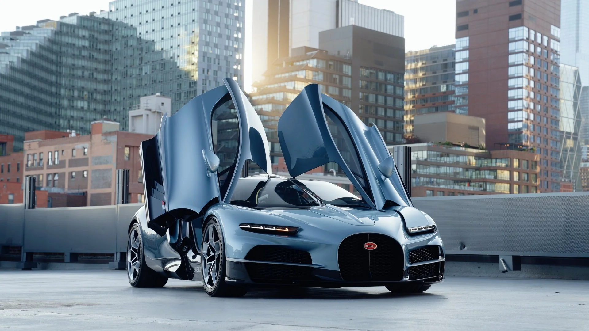 A Bugatti Tourbillon with doors open, parked in an urban rooftop setting with city skyscrapers in the background.