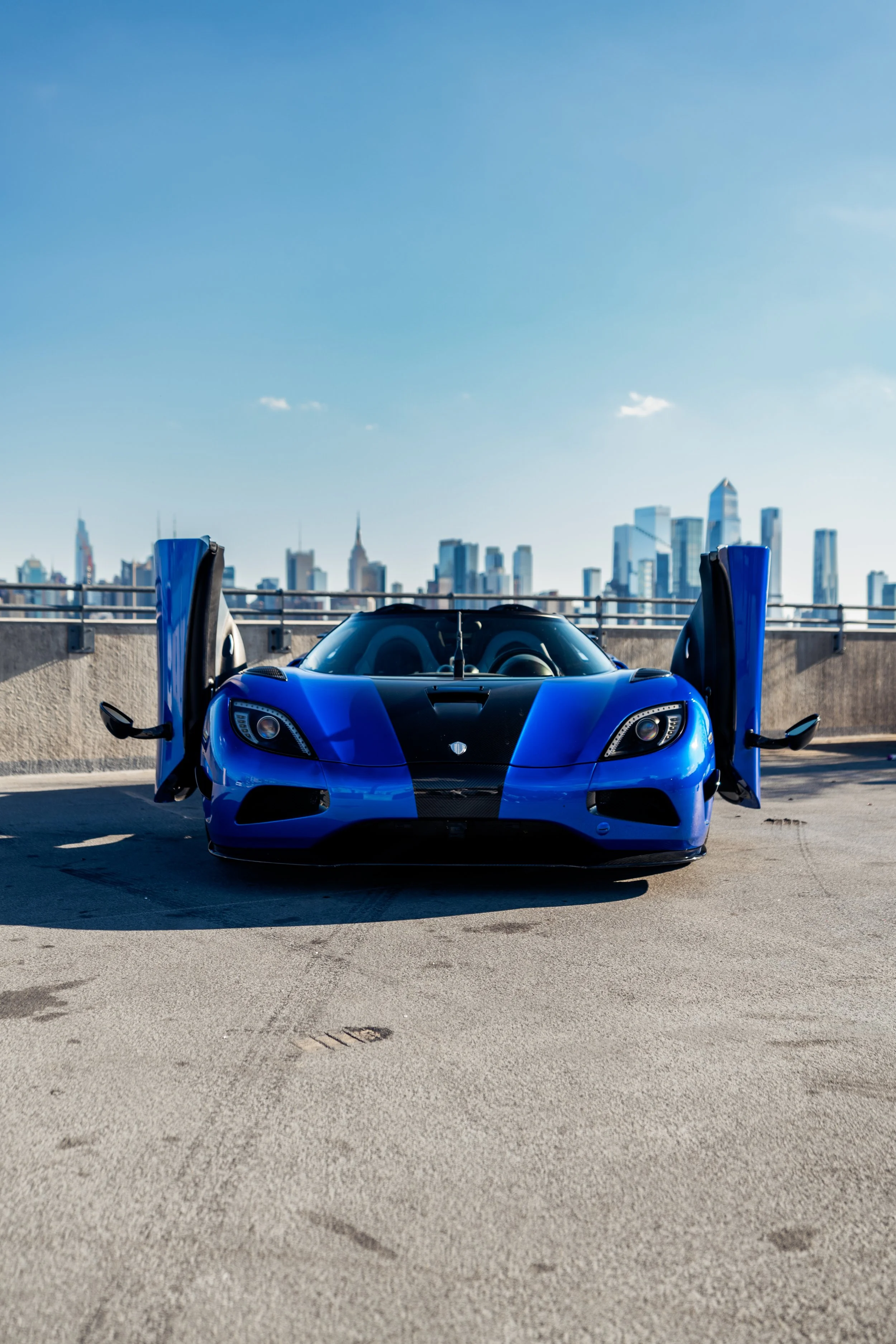 A Koenigsegg Agera S "HH" with its gullwing doors open parked on a rooftop parking lot with a city skyline in the background.