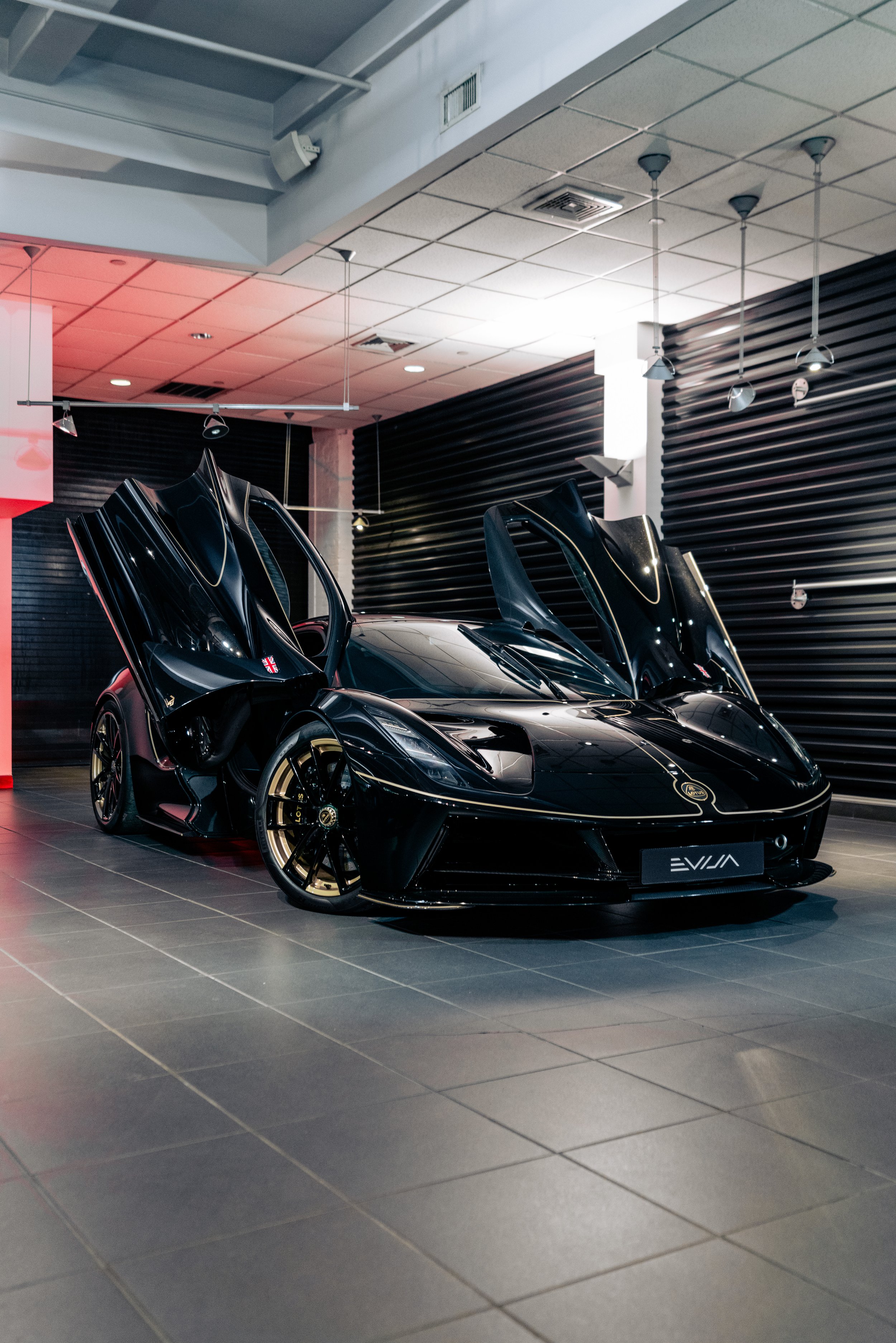 Black luxury sports car with gull-wing doors open inside a showroom with black wall panels and tiled floor.