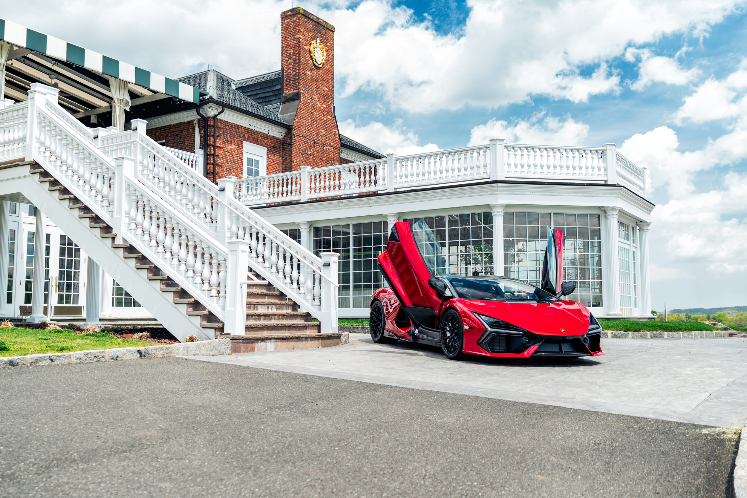 Lamborghini Revuelto with doors open parked in front of a white house with a brick chimney and staircase.
