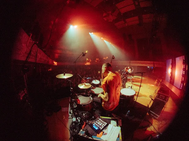Drummer on stage during a live concert performance with red lighting