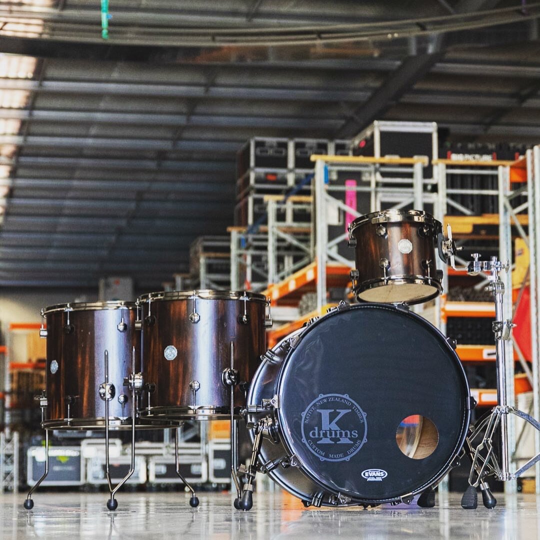 A brown drum kit set up in a warehouse with shelves in the background.