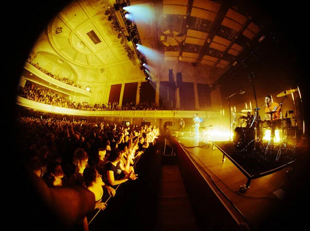 Concert in a large indoor hall with audience and performers on stage, fisheye lens view.