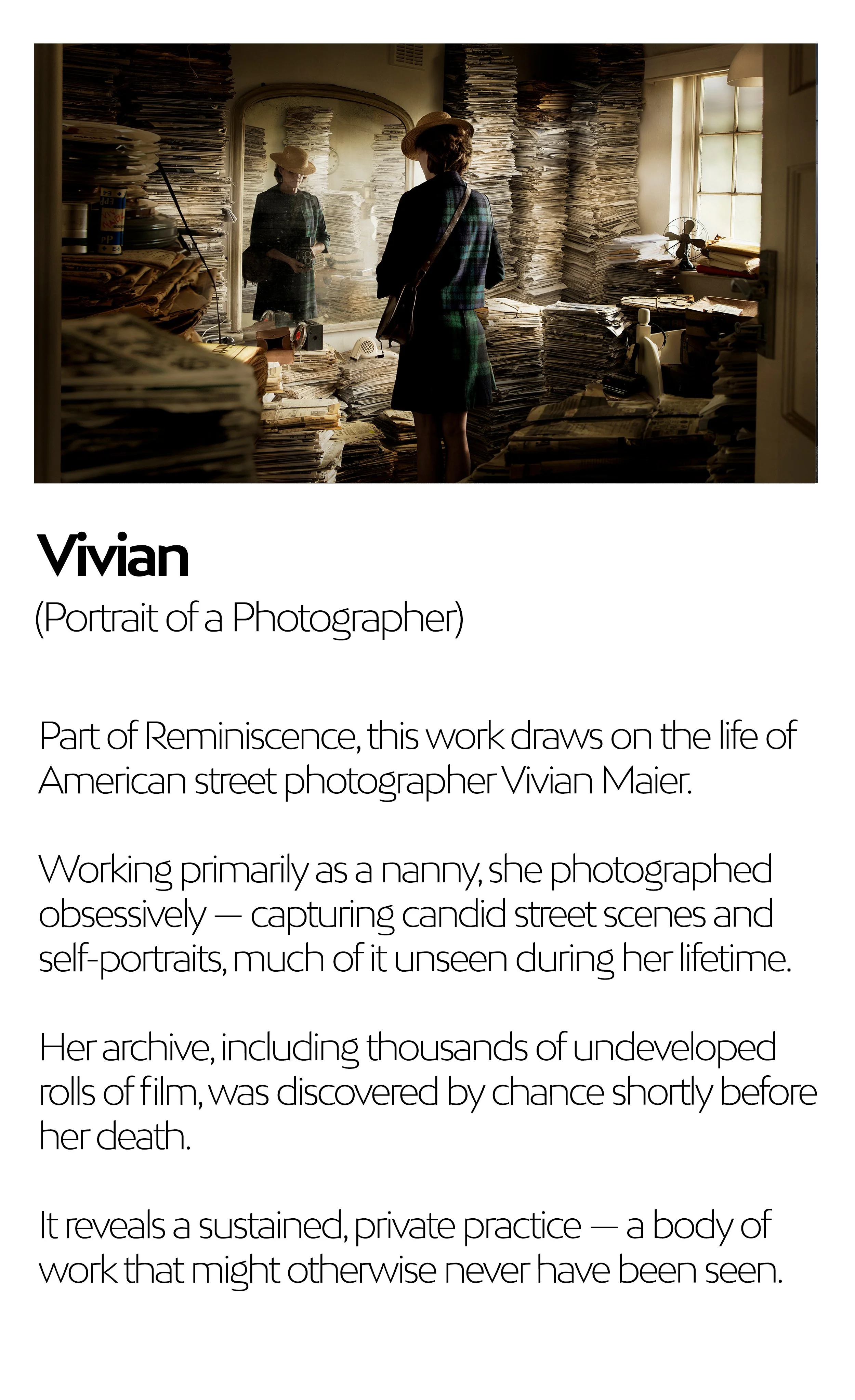 A woman standing in front of a mirror in a cluttered room filled with stacks of paper and shelves of rolls of film, illuminated by natural light from a nearby window.