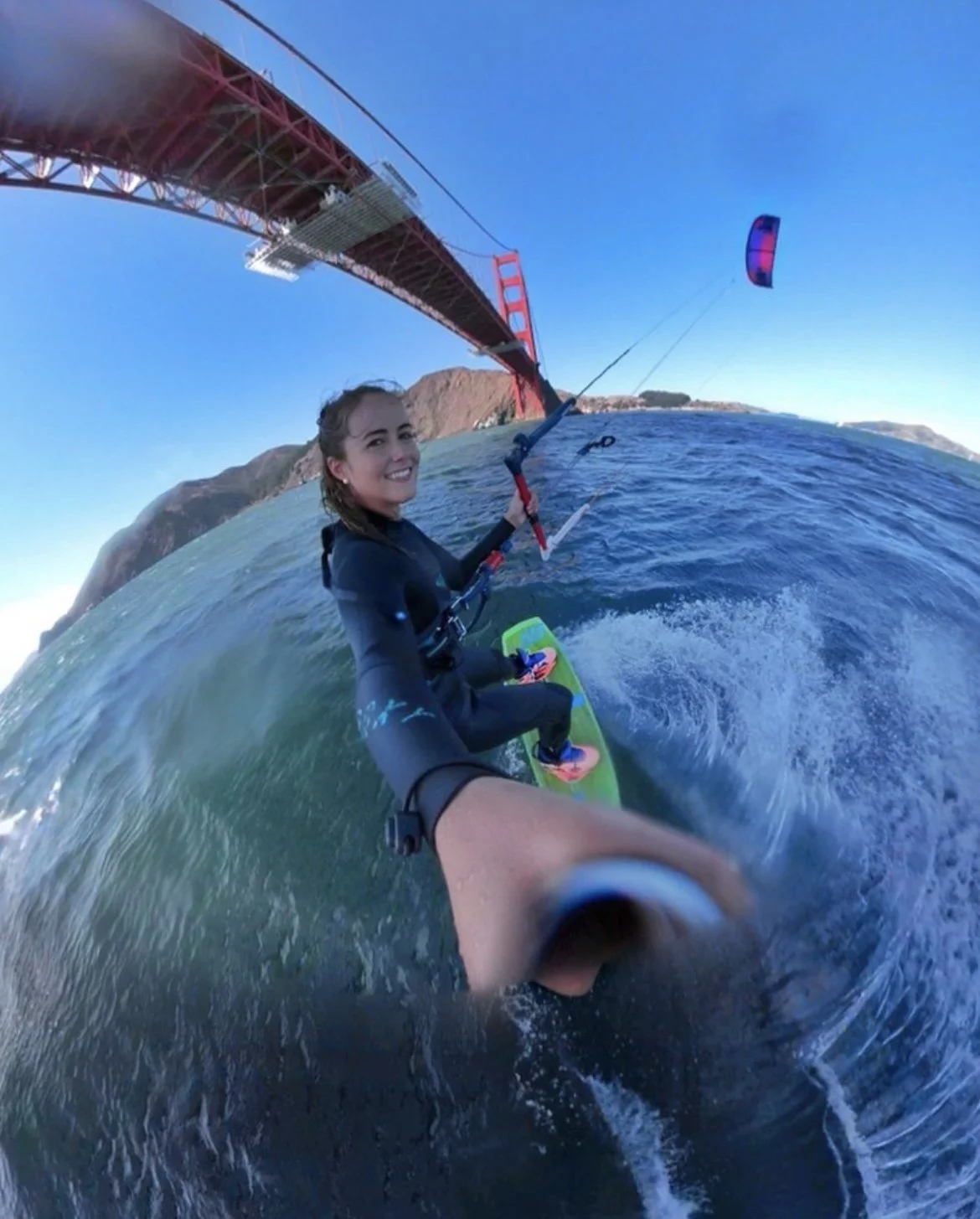 Woman kiteboarding under the Golden Gate Bridge in San Francisco on a sunny day.