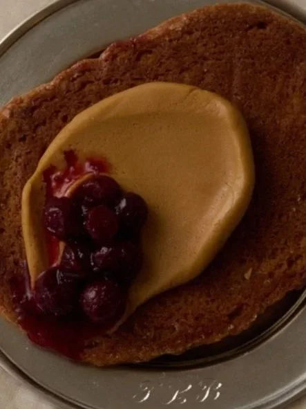 galette topped with a dollop of compote and maple butter, mixed berries, served on a plate.
