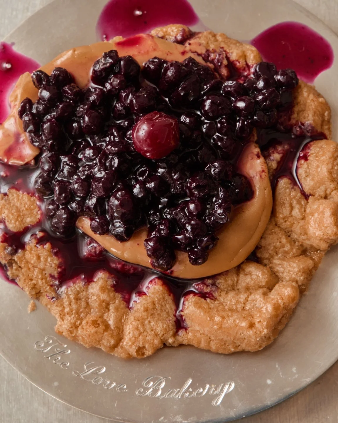 a galette topped with cream and dark berries, on an engraved silver tray.