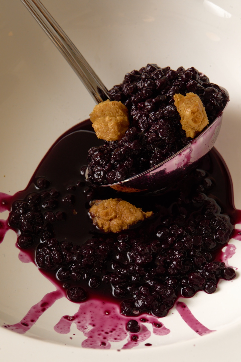 a spoon lifting dark berry compote from a white bowl.