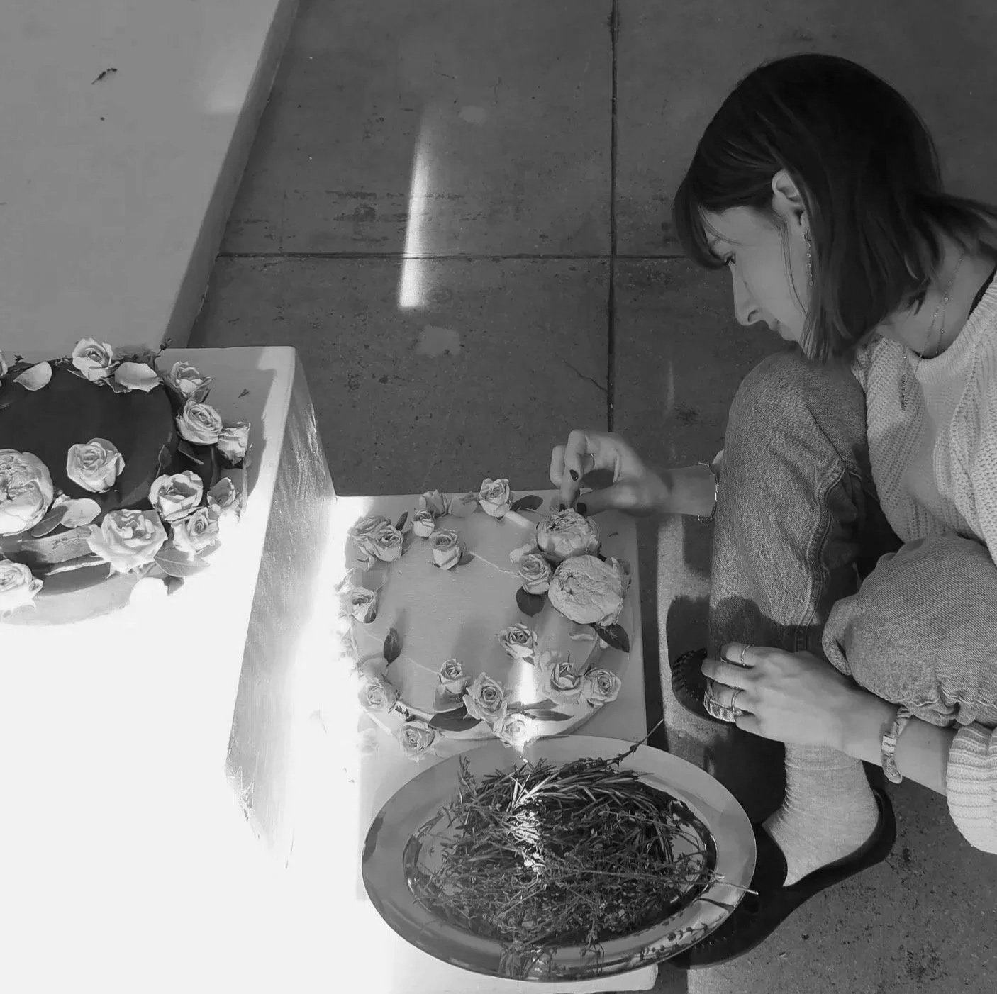 Erica sitting on the ground, arranging flowers and roses on a table, with a cake decorated with roses nearby.