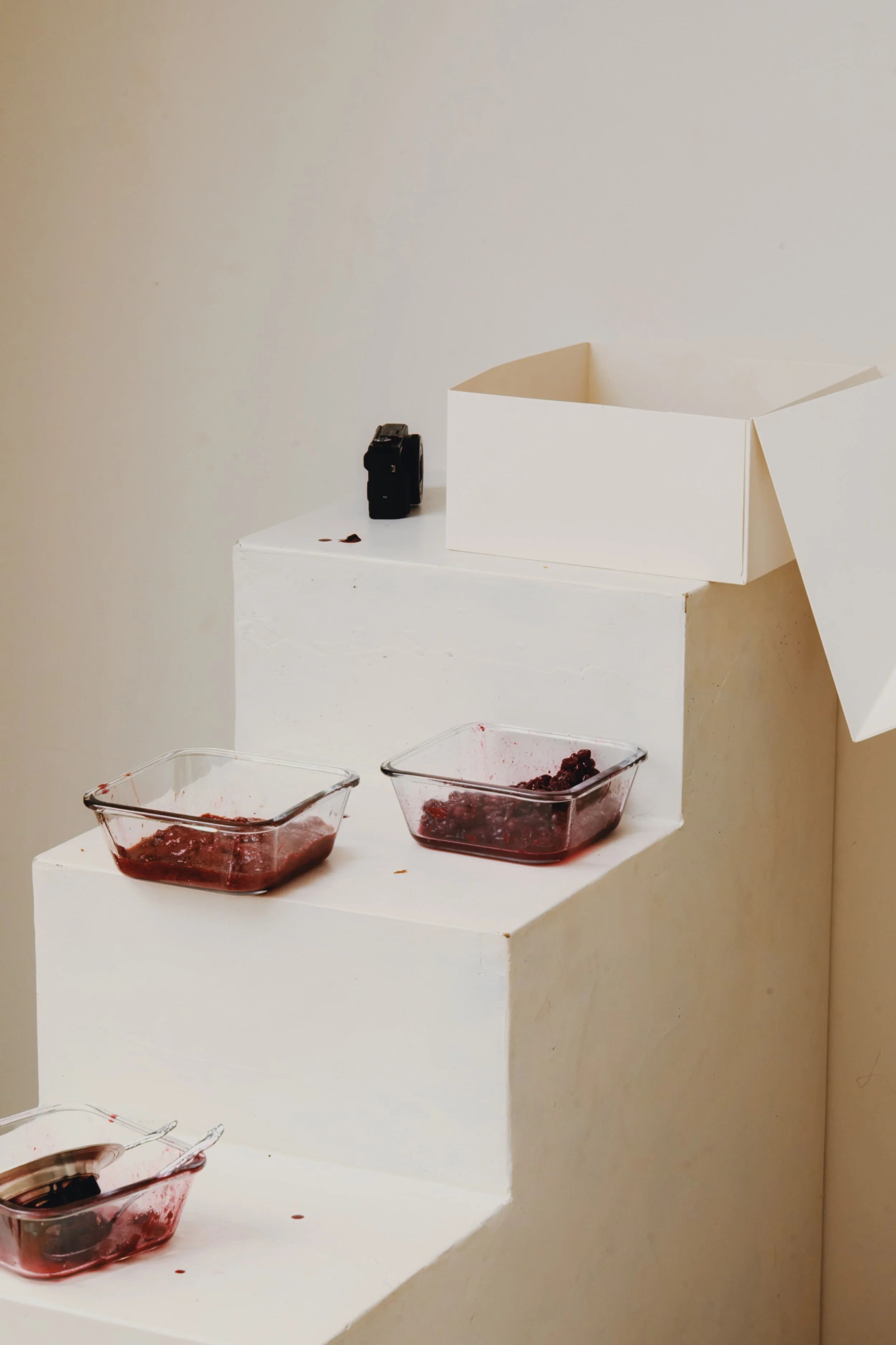 glass dishes of berry compote on white steps, in a pale room.