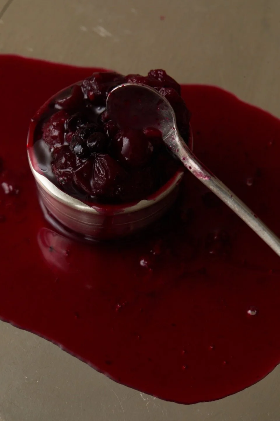 a silver cup of dark berries with a spoon, compote pooling on silver.