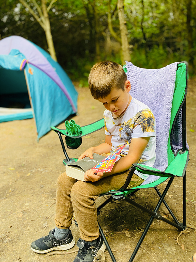 A child reading beside a tent at Fire and Stars
