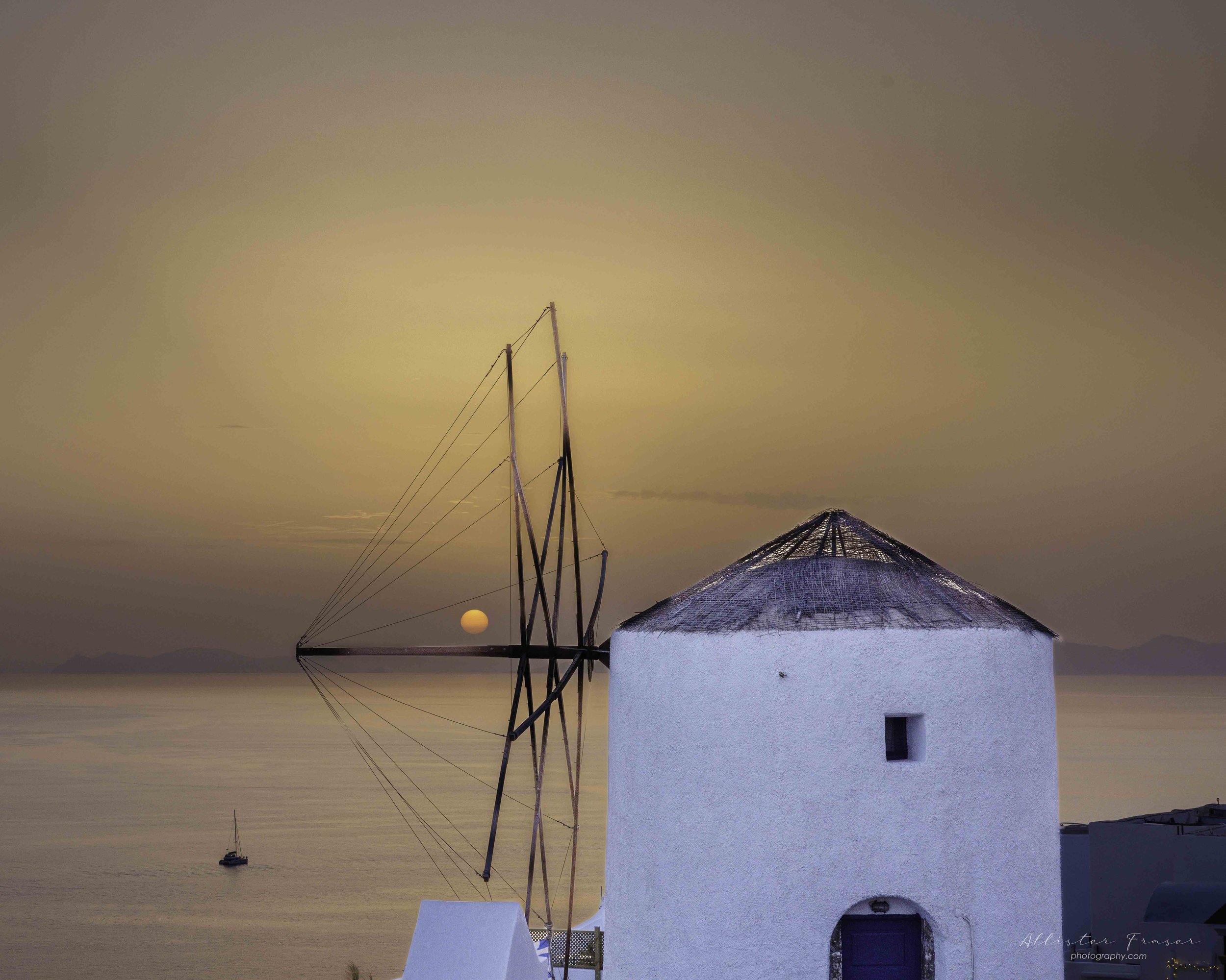 sun setting on the horizon above the Oia windmill