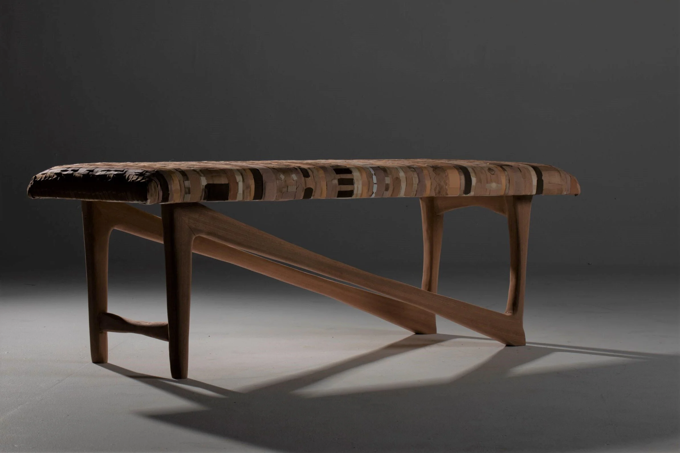 A wooden bench with a patterned, multicolored cushioned seat against a dark background.