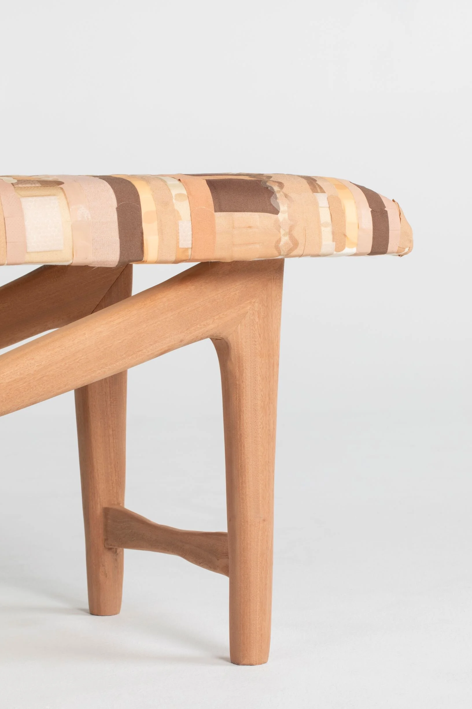 Close-up of a wooden stool with a fabric seat cushion in neutral tones against a white background.