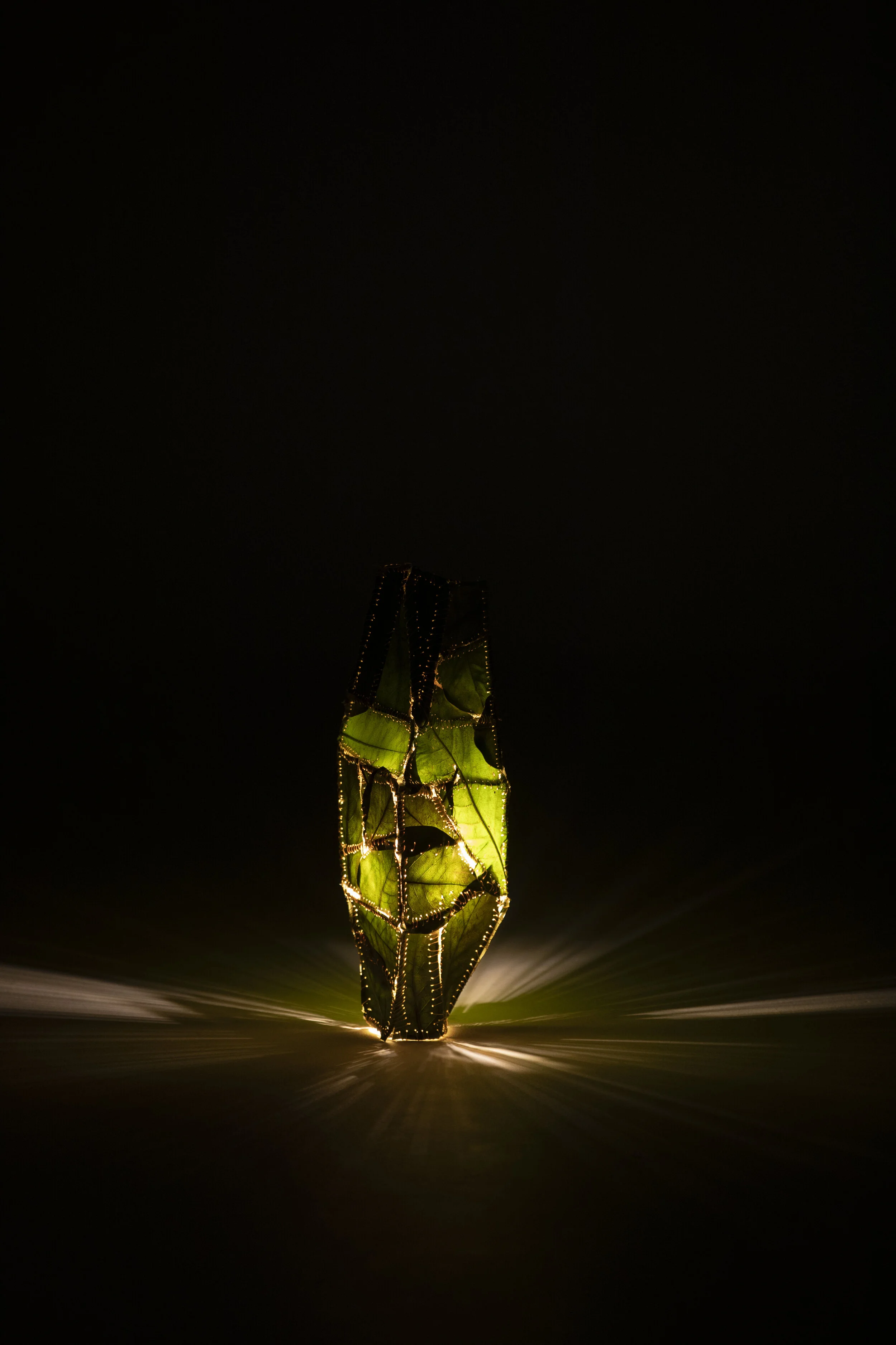 A glowing green and black paper lantern with intricate cutout patterns, illuminated from within, resting on a dark surface.