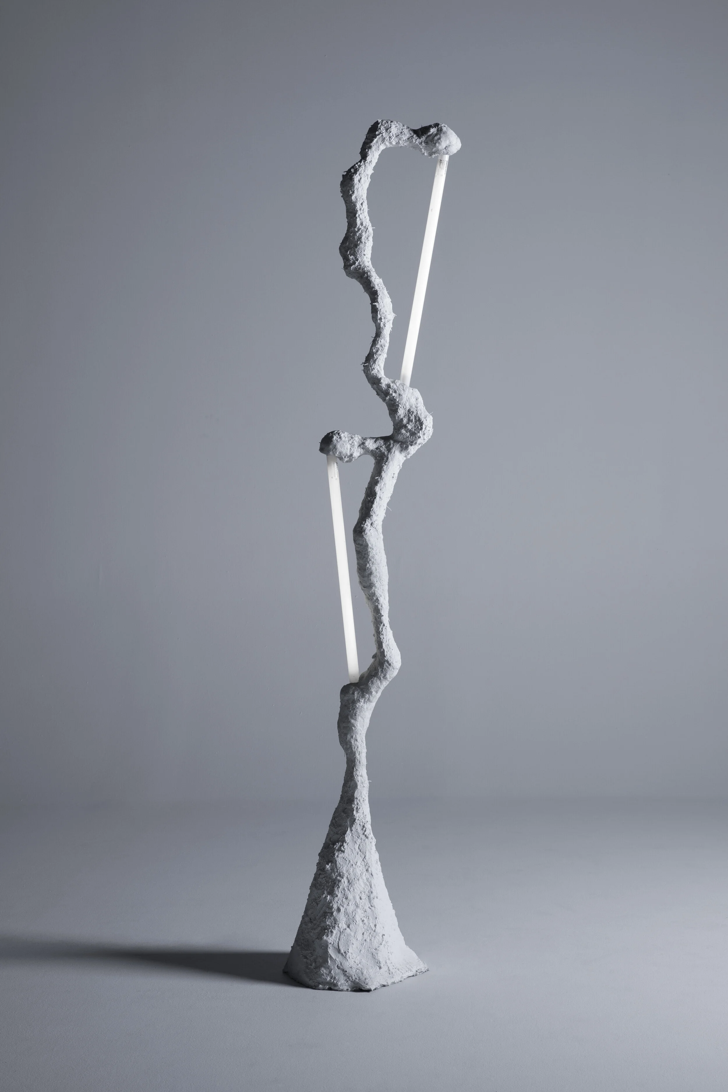 Contemporary abstract sculpture consisting of a rough, irregular white base with two white rods extending through a twisted, textured gray form.
