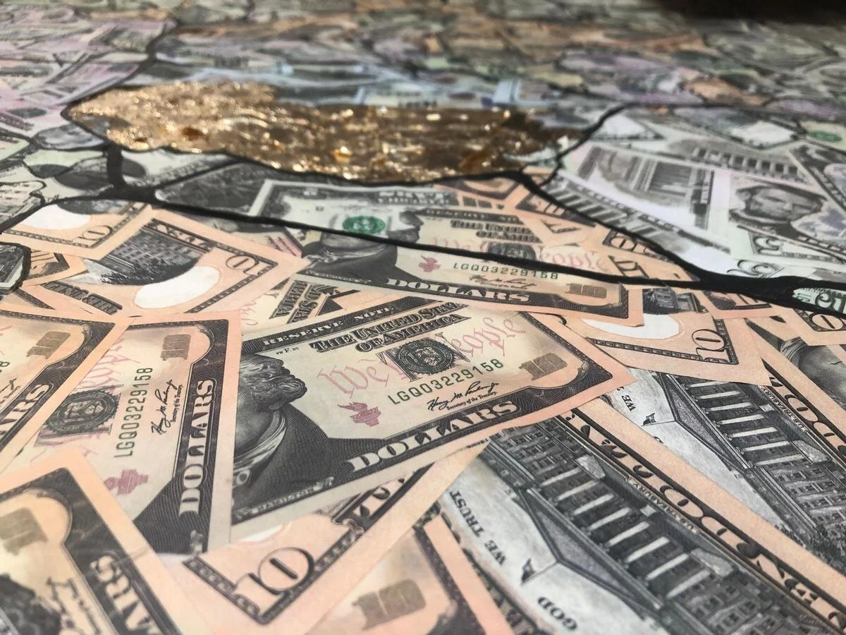 A pile of scattered US $50 and $10 bills with a gold-colored decorative object and a black string on top.