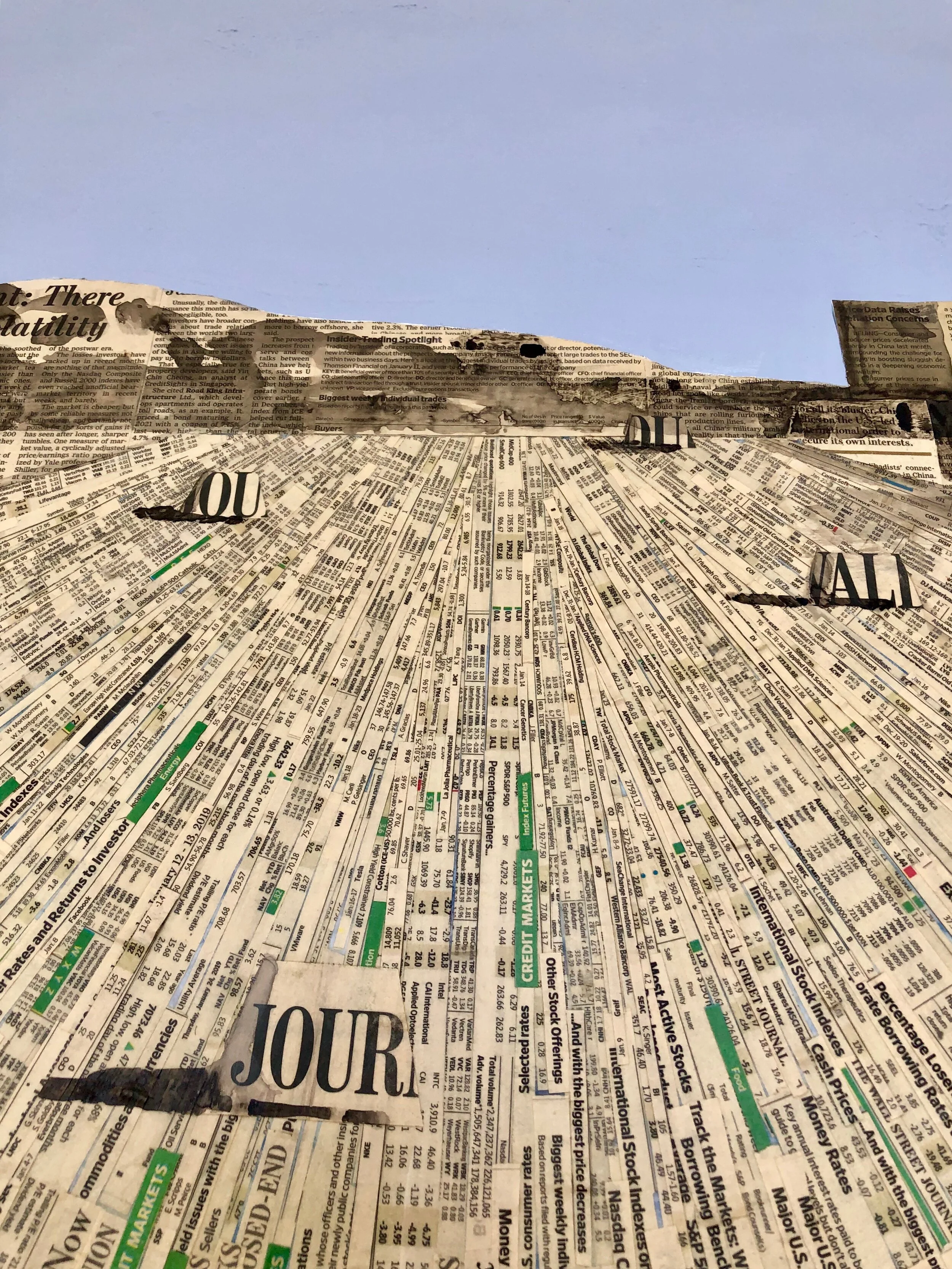 A surface covered with torn pieces of newspapers, with a blue sky visible in the background.