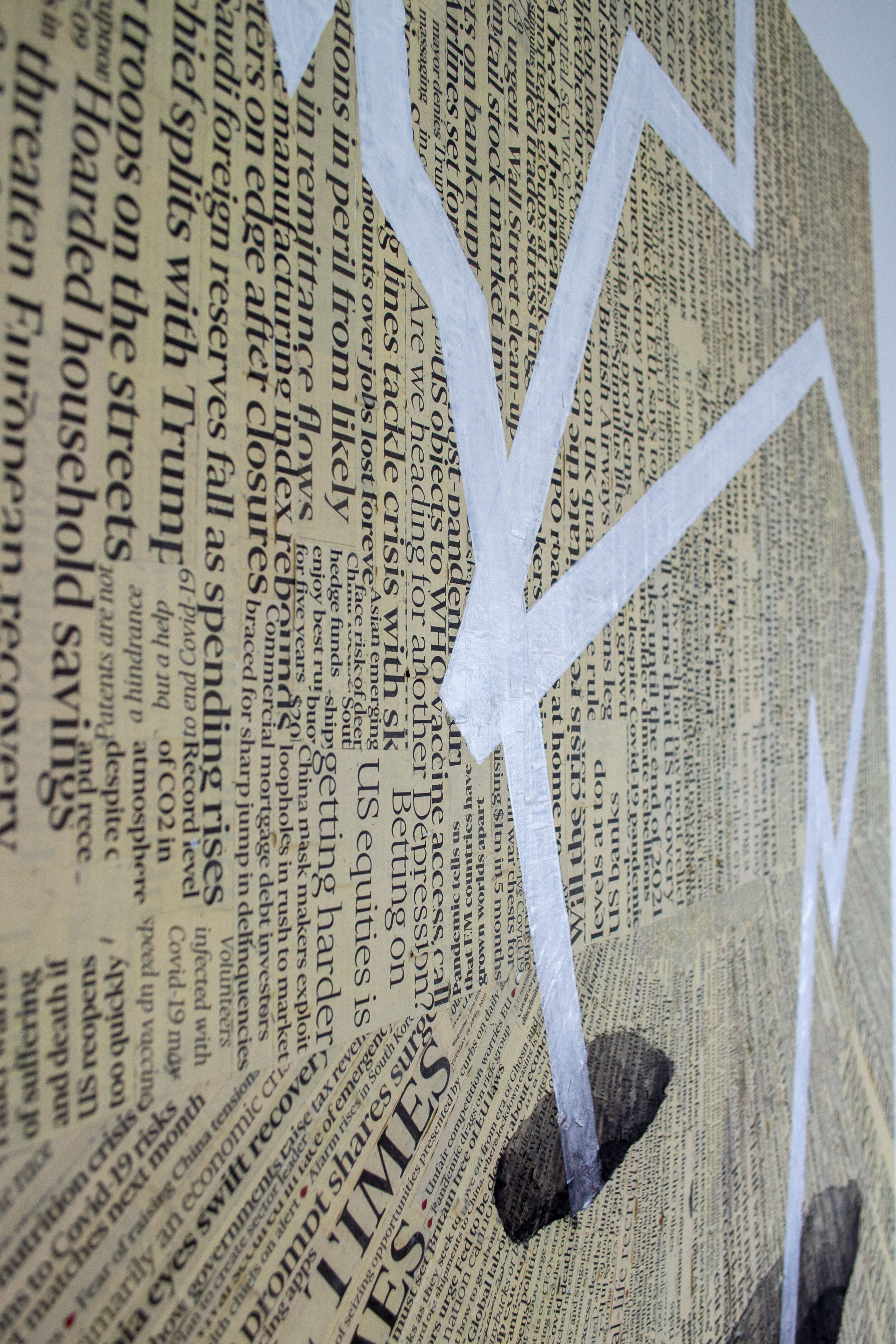 A newspaper article with a white and gray checkmark symbol painted on top, and some rocks at the base of the wall.