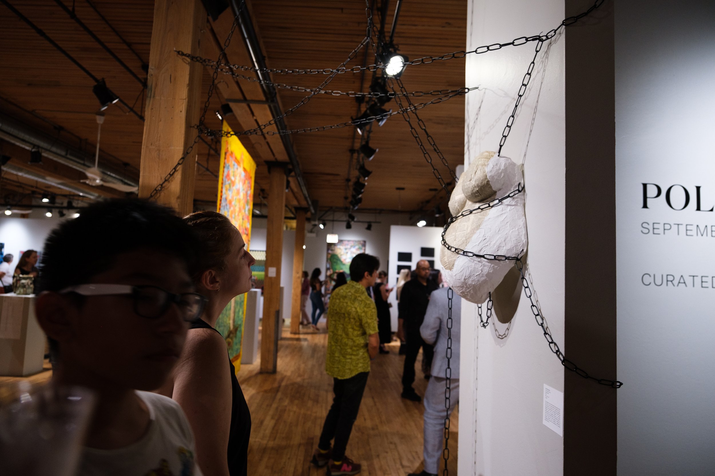 People viewing artwork at an art gallery, with chain-link arrangements around a sculpture on the wall.