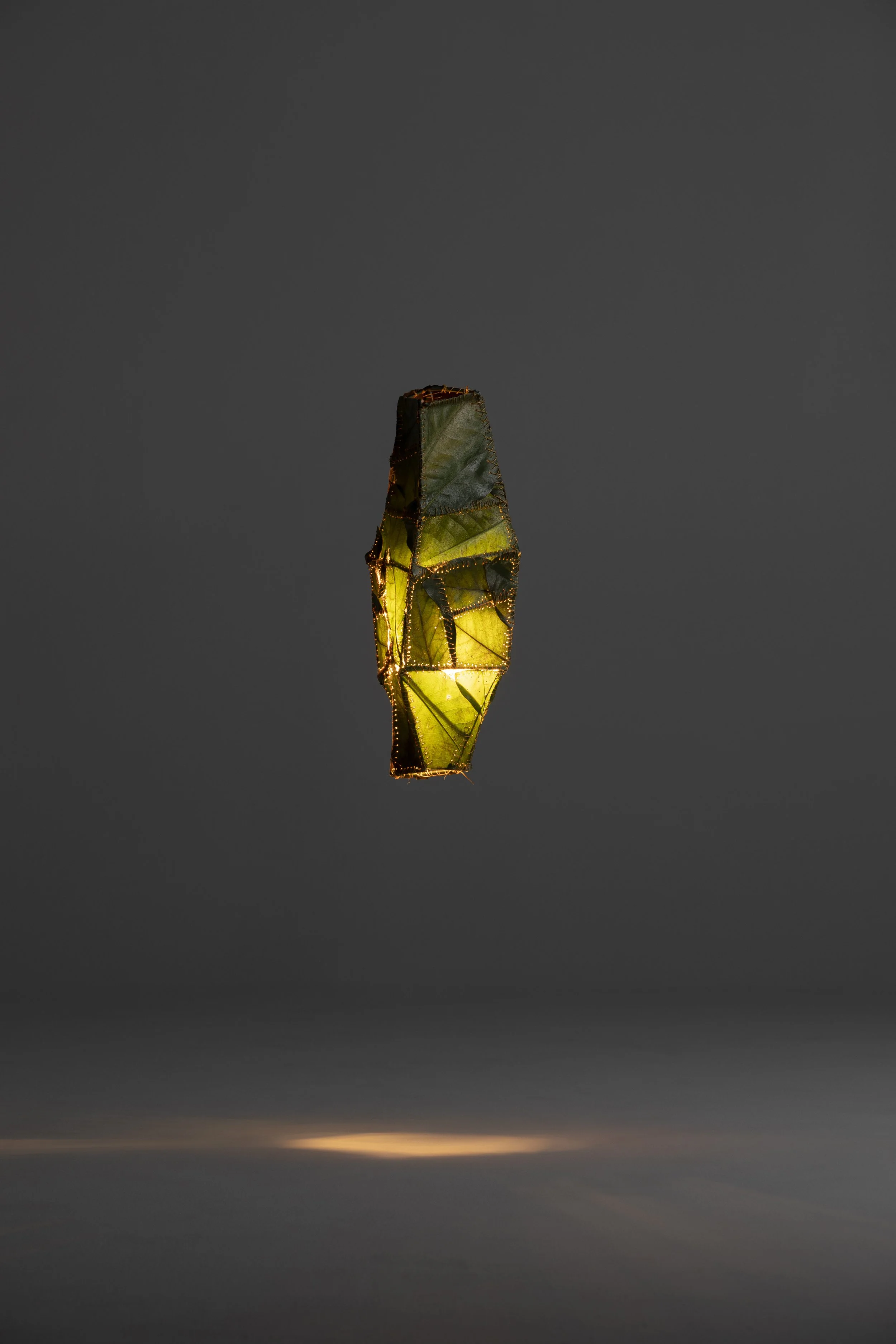 A glowing, geometric lantern floats against a dark background, illuminating with yellow and green hues.