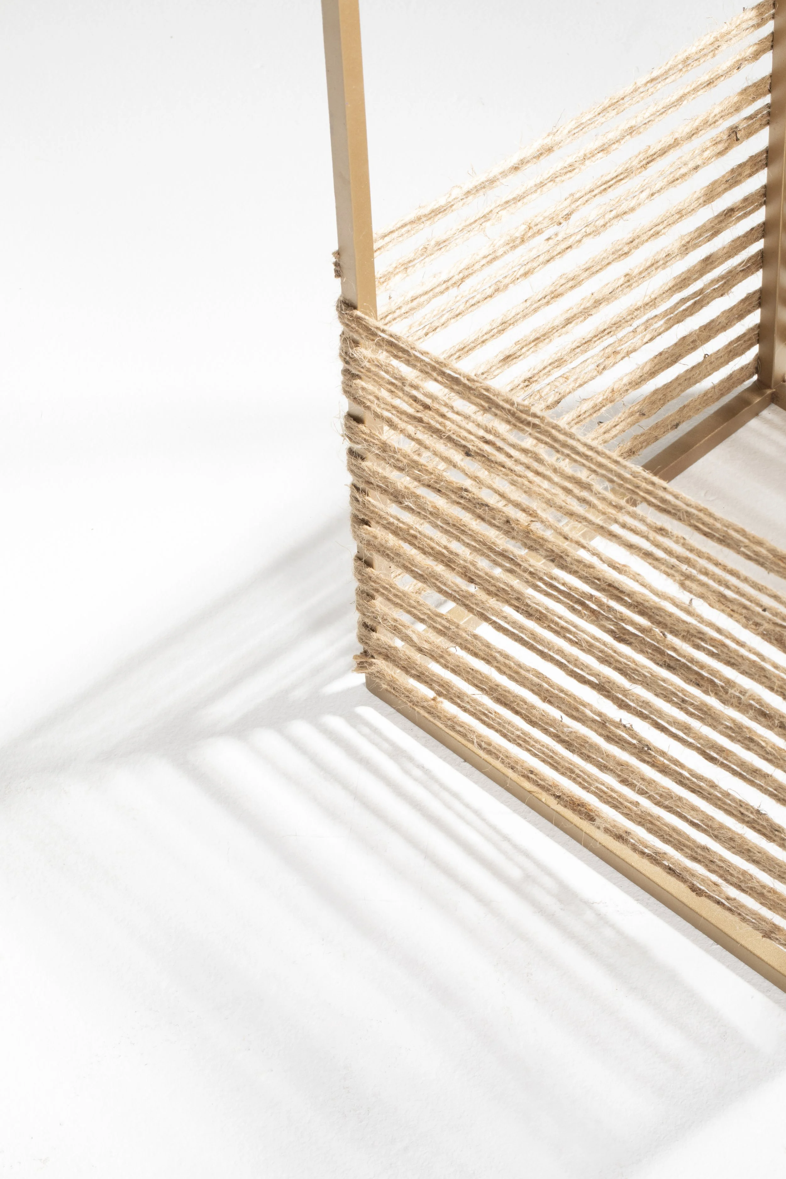 A decorative wooden frame with horizontal string or twine wrapped around the bottom corner, casting shadows on a white surface.