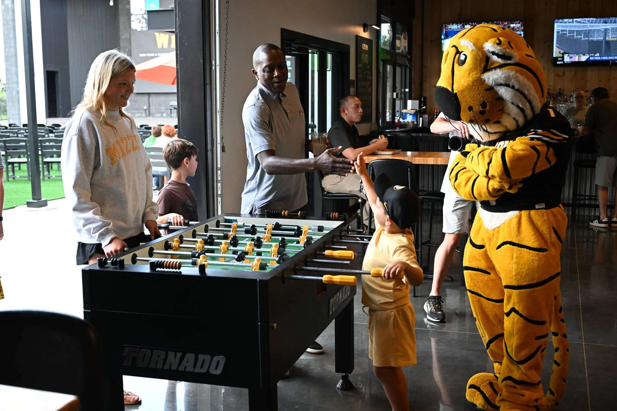 Banner Sharbaugh, 4, gives a high five to Mizzou men’s head basketball coach Dennis Gates while playing Madison Elliot, 17, in foosball at the Zou to You event on Wednesday, June 24, 2026, at the Kitchen Bar and Grill in Columbia. Banner is the son o