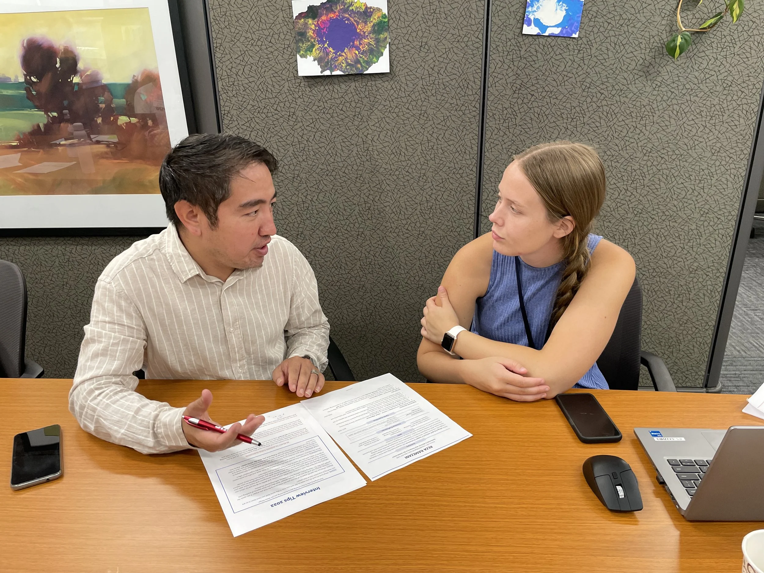 Two people sitting at desk talking over papers.