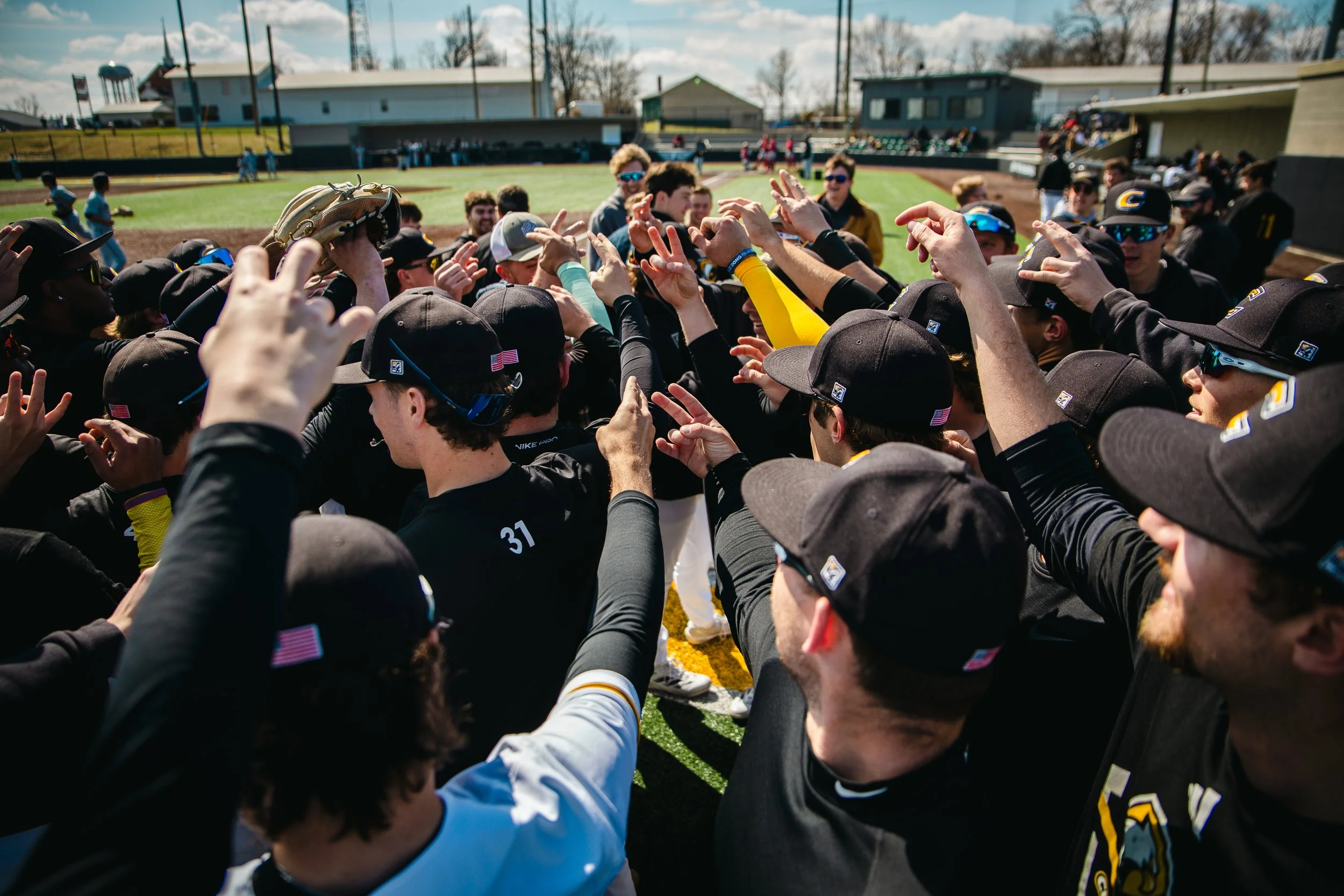A baseball team in black uniforms and caps gathered in a huddle on the field.
