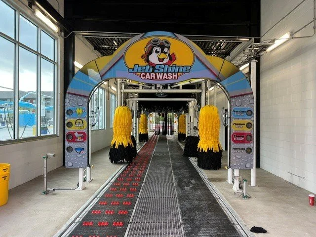 Indoor car wash station at Jet Shine Car Wash with yellow and black brushes and a cartoon dog logo above.