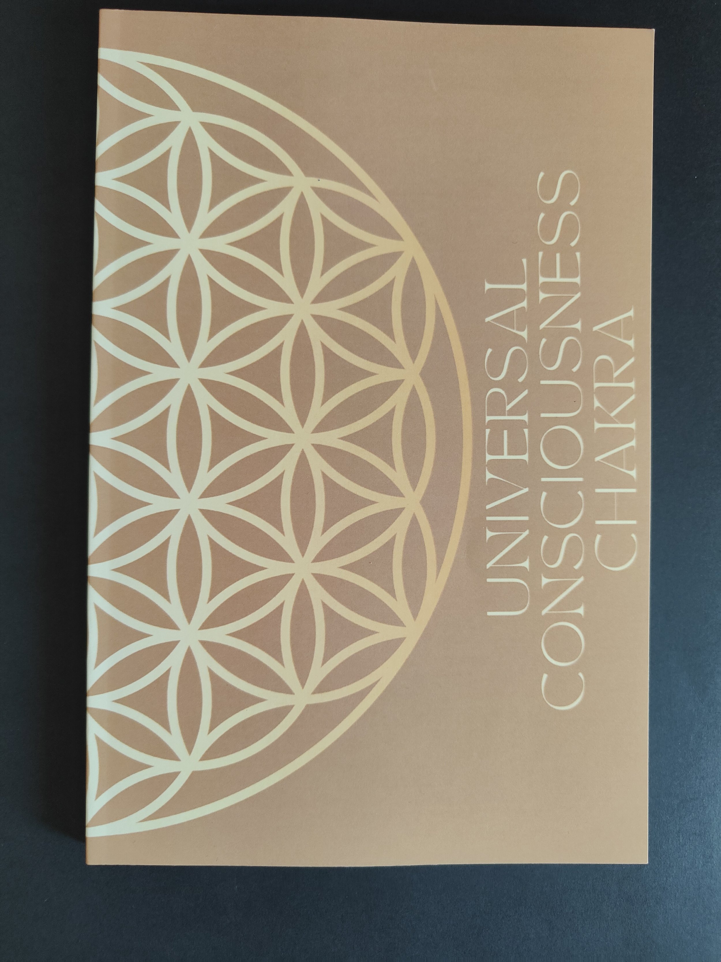 A tan card with a white geometric flower of life pattern on the left side and the text "UNIVERSAL CONSCIOUSNESS CHAKRA" on the right side.