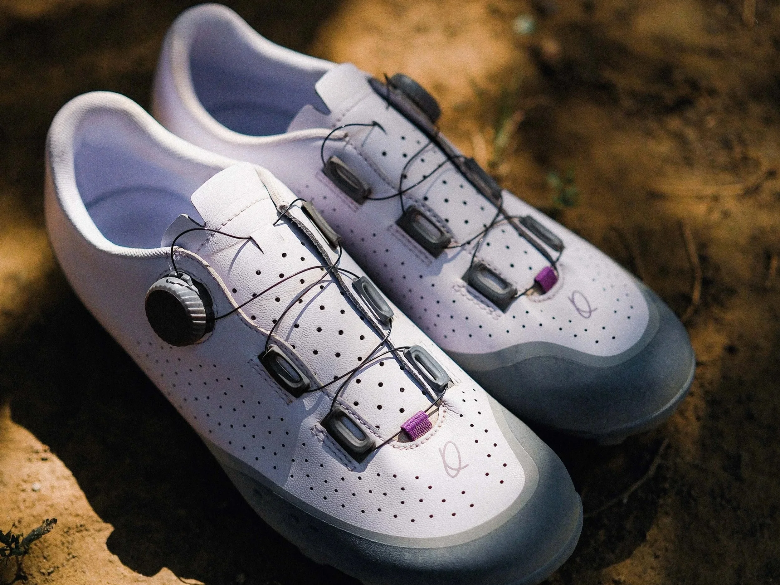 Close-up of cycling shoes on a gravel trail, with person's legs wearing black socks and beige cycling shoes with a dial lock system.
