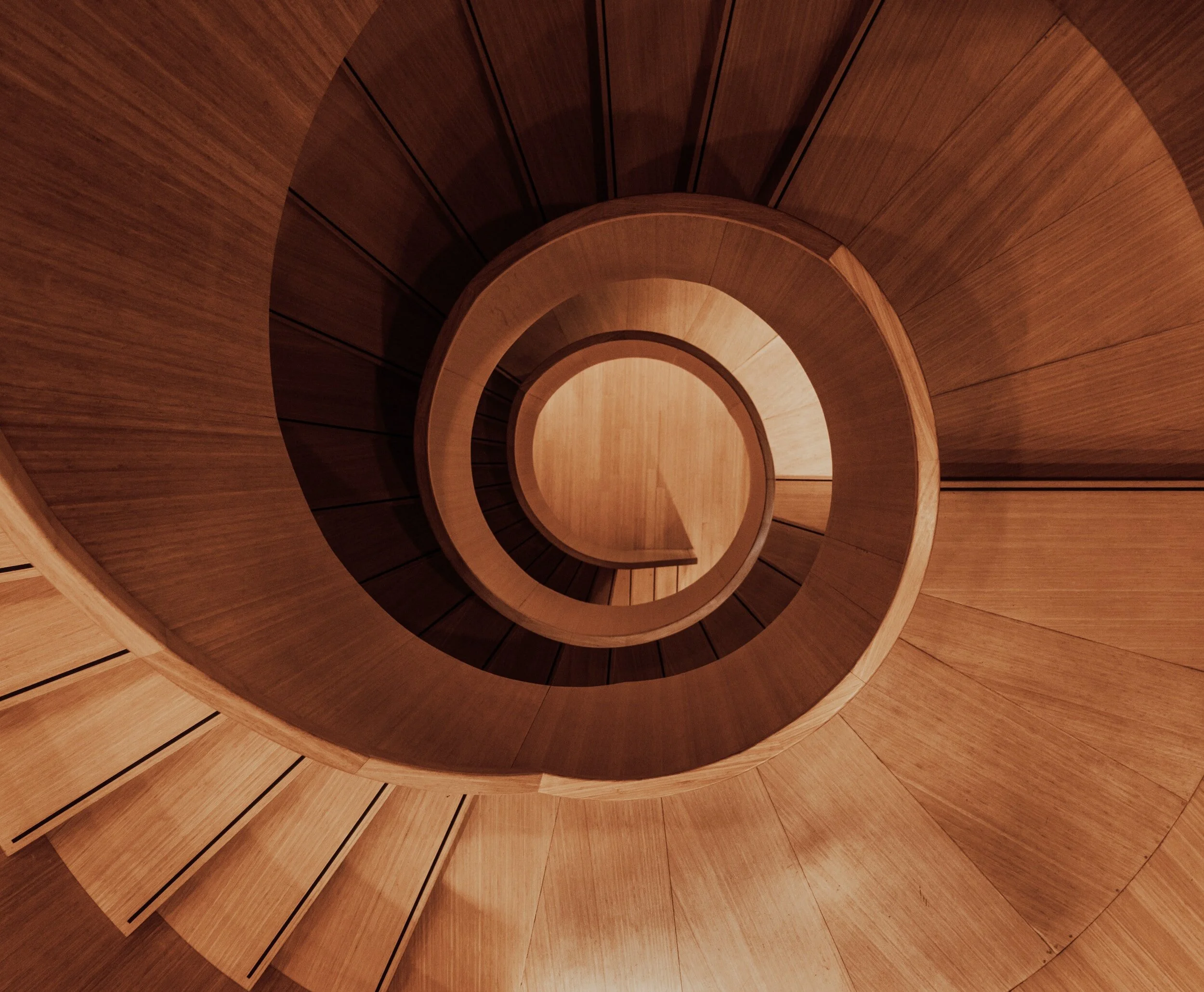 Looking down a wooden spiral staircase from above, capturing the circular design and warm wood tones.